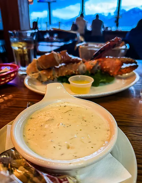 Close-up of a bowl of salmon chowder with a plate of crab legs and drawn butter in the background at The Hangar restaurant in Juneau, Alaska.