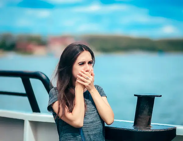 A woman on the deck of a boat covering her mouth, appearing seasick or uncomfortable while near the water