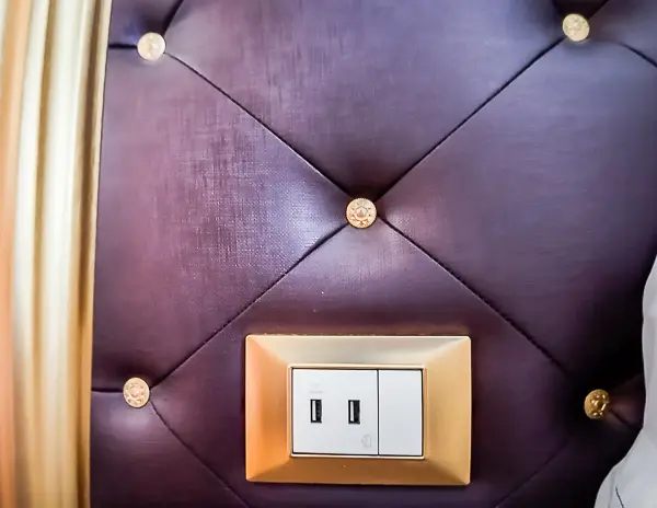 A close-up of the padded headboard in Carnival Firenze Ocean Suite 7359 with two built-in USB-A ports on one side of the bed.