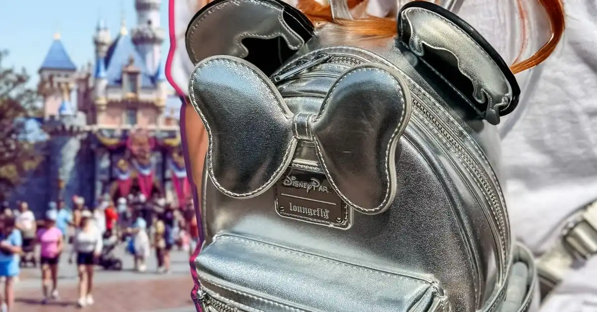 featured image: Close-up of a silver Disney Loungefly backpack with mouse ears and bow in front of Sleeping Beauty Castle, representing a Disneyland packing list for adults.