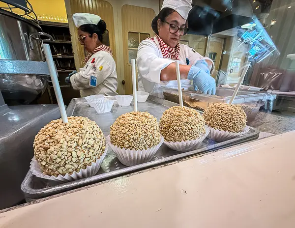 Caramel apples coated in crushed peanuts at Disneyland, with a candy maker working behind the counter.