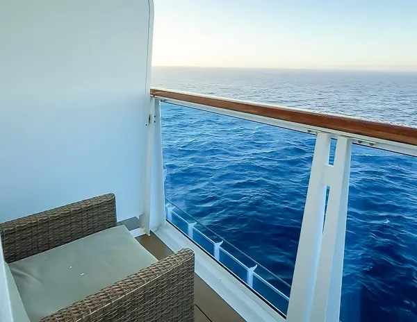 Balcony of Carnival Firenze Ocean Suite 7359 with a wicker chair facing the open ocean.
