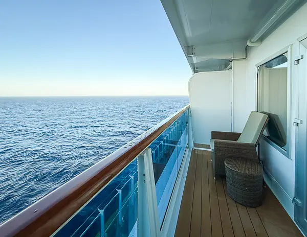 Spacious balcony of Carnival Firenze Ocean Suite 7359 with two wicker chairs and a side table, overlooking the ocean.