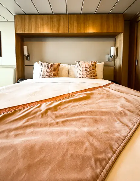 Overhead storage cabinets above the bed in a Celebrity Solstice Class cruise cabin, ideal for keeping extra clothes, shoes, or a laundry bag out of sight.