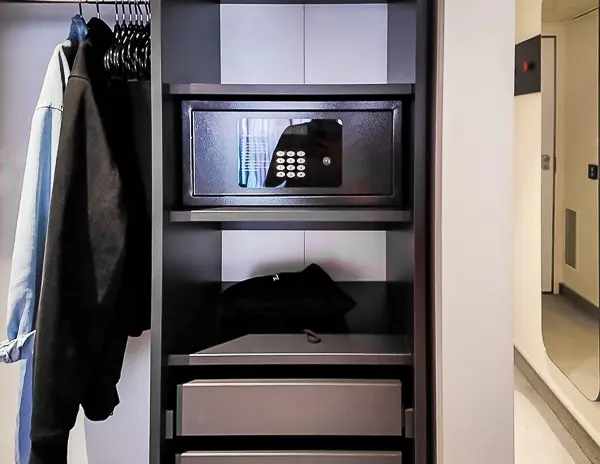 Cruise ship cabin closet with a built-in safe, shelves, and hanging clothes for organized storage.