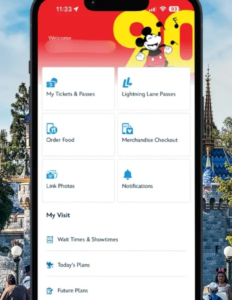 Smartphone screen showing the Disneyland app home page with options for tickets, Lightning Lane passes, mobile food ordering, and more, with Sleeping Beauty Castle blurred in the background