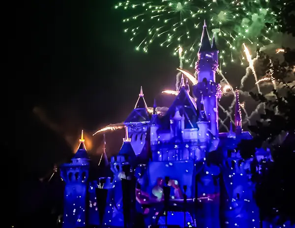 Sleeping Beauty Castle at Disneyland illuminated in blue with fireworks exploding in the night sky above.