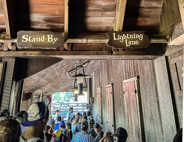 Entrance signs for the Stand-By and Lightning Lane queues at a Disneyland attraction, with guests waiting in line.