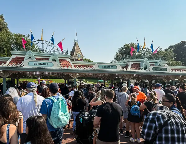 Crowds waiting in line at the entrance gates to Disneyland on a sunny morning.
