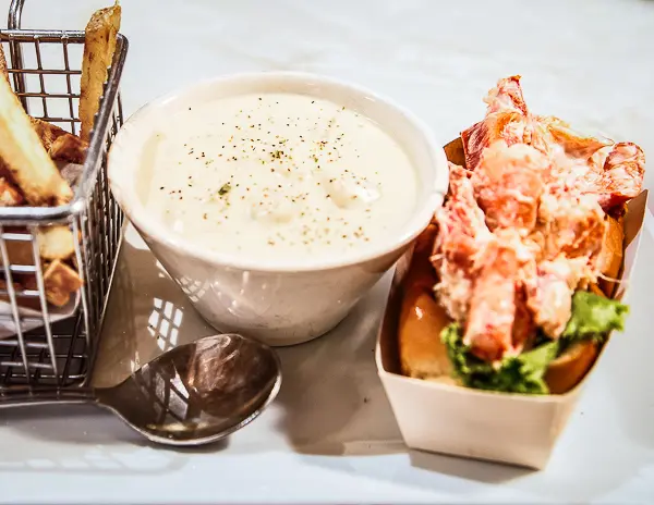 Bowl of New England clam chowder with a lobster roll and fries, a classic fall meal in Maine