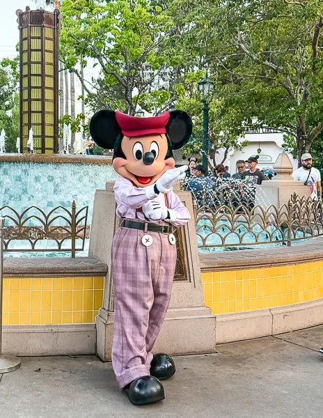 Mickey Mouse posing in a vintage-style outfit near a fountain at Disney California Adventure