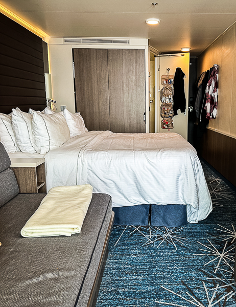 Organized cruise ship cabin with bed, sofa, hanging clothes, and an over-the-door organizer, showing how unpacking and creating zones can make a small cabin feel more spacious.
