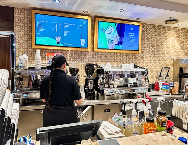 Barista preparing drinks at Royal Caribbean’s onboard café with espresso machines, coffee syrups, and digital menu screens.