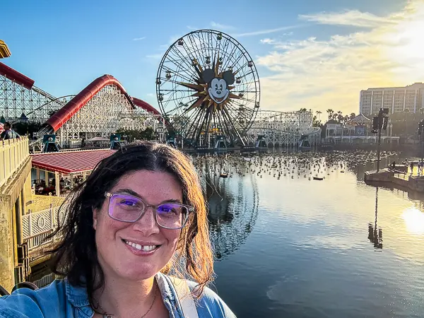 Woman (kathy) taking a selfie at Pixar Pier in Disney California Adventure with the Pixar Pal-A-Round Ferris wheel in the background at sunset.