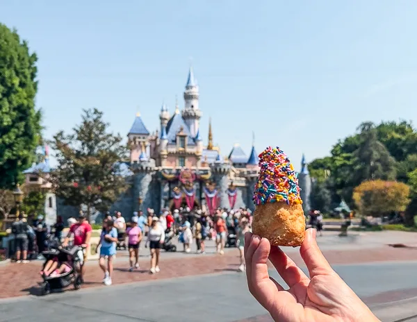 Hand holding a Matterhorn Macaroon topped with colorful sprinkles in front of Sleeping Beauty Castle at Disneyland.
