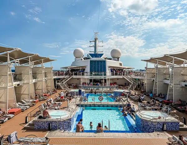 Cruise ship pool deck with lounge chairs, hot tubs, and passengers relaxing in the sun — a popular spot where chair hogging can become an issue.