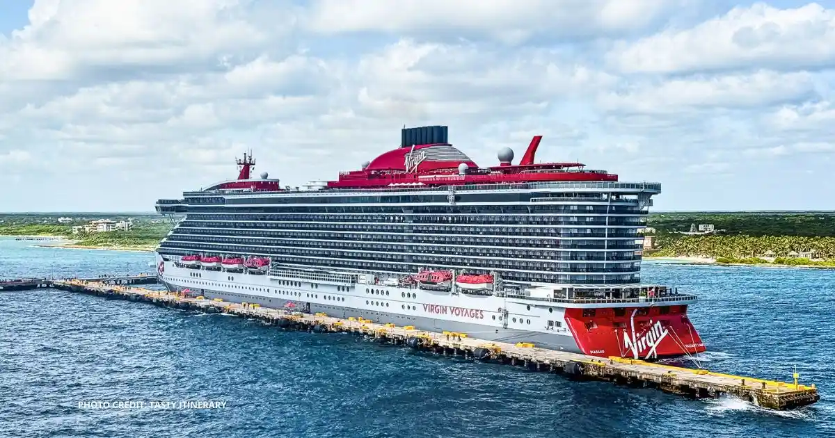featured image: Virgin Voyages cruise ship docked at port on a sunny day, showing the red funnel with the Virgin logo and the ship’s name along the hull.