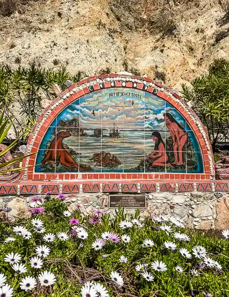 Bay of Seven Moons tile mural in Avalon, Catalina Island, surrounded by flowers and set against a rocky hillside.