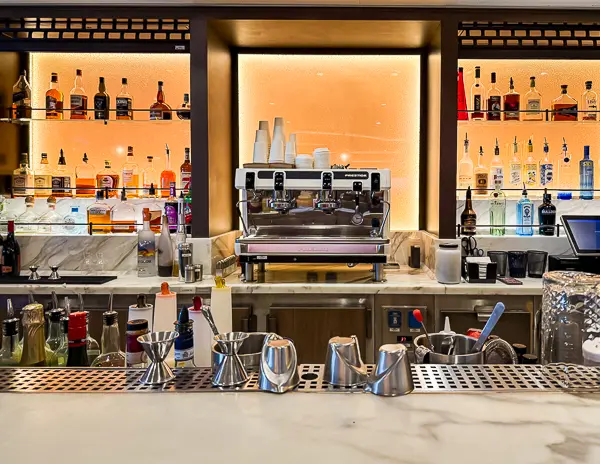 A Carnival cruise ship bar with liquor bottles and an espresso machine on display, showcasing the variety of beverages included in Carnival drink packages.
