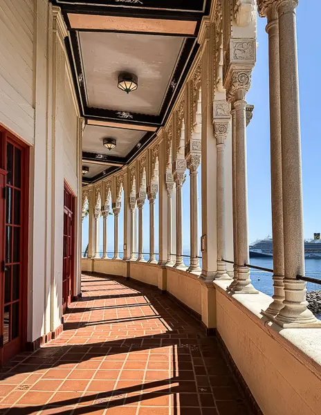 Terrace walkway at the Catalina Casino with ornate columns overlooking the harbor and a cruise ship in the distance