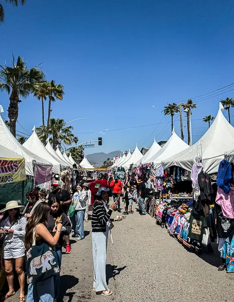 Street market outside Cruiseport Village in Ensenada, Mexico, along Blvd. Lázaro Cárdenas, with white vendor tents selling souvenirs and food as cruise passengers walk through.