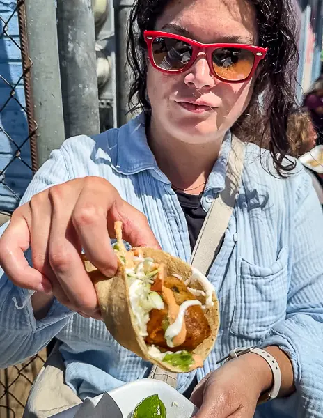 Woman (Kathy) holding a freshly made fish taco in Ensenada, Mexico, topped with cabbage, salsa, and crema on a corn tortilla.