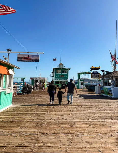 Family walking on the Green Pleasure Pier in Avalon, Catalina Island, with the Fish and Chips stand and ticket booths in view.