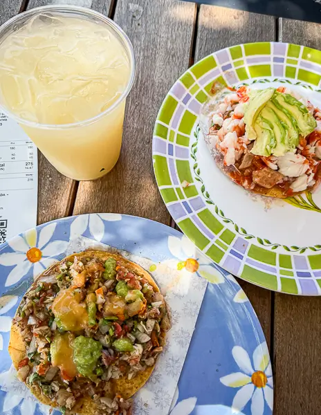 Two seafood tostadas from La Guerrerense in Ensenada, Mexico, one topped with shrimp and avocado and the other a campechana mix of seafood ceviche, served with an agua fresca.