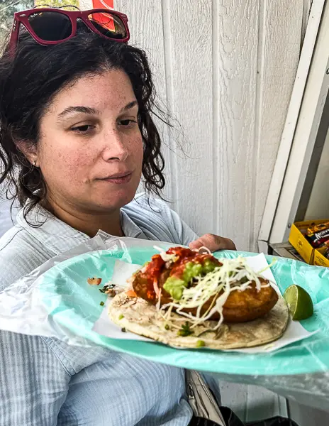 Woman (Kathy) holding a fish taco from Tacos Corona in Ensenada, topped with cabbage, salsa, and crema.