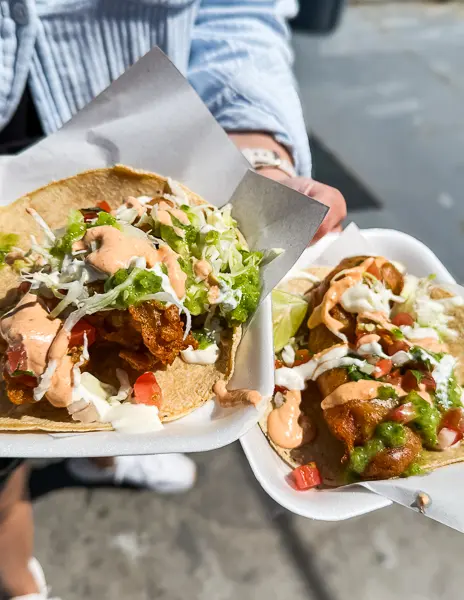Two tacos from Tacos Fenix in Ensenada, Mexico, one fish taco and one shrimp taco, topped with cabbage, salsa, and crema on corn tortillas.