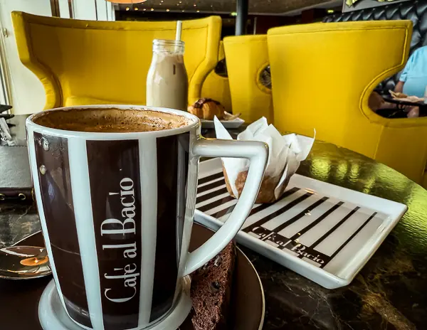 Cappuccino served at Café al Bacio on a Celebrity Cruise ship, with biscotti and pastries on the table in the café’s signature setting.