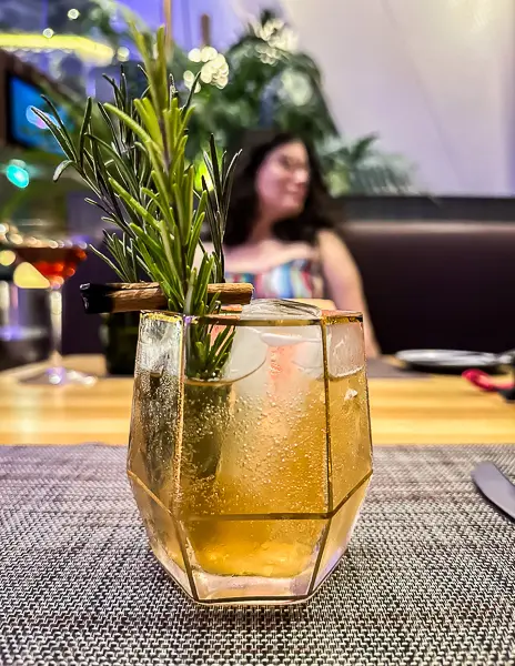 Creative cocktail garnished with rosemary and cinnamon on a Celebrity Cruise ship, served in a geometric glass at dinner.
