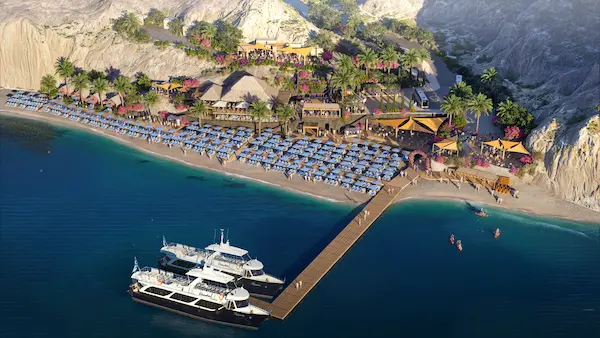 Aerial rendering of Royal Beach Club Santorini, showing yachts docked at a wooden pier, rows of blue lounge chairs and umbrellas along the beach, and palm-lined areas with cabanas and open-air dining spaces built into the rocky hillside. Image courtesy of Royal Caribbean.