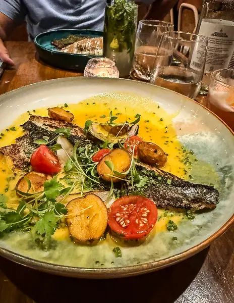 Pan-seared branzino with crispy skin, cherry tomatoes, potatoes, and microgreens in a bright yellow sauce at Lima Bistro in Aruba. 