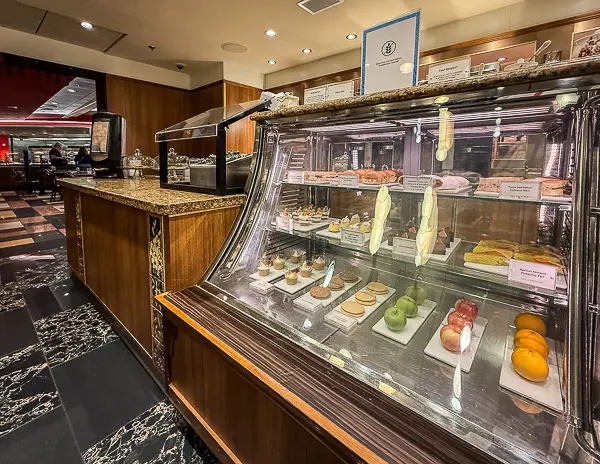 Pastry display case at Café Promenade on Quantum of the Seas, filled with small desserts, cookies, and pastries, with the café’s marble floors and serving counters visible in the background.