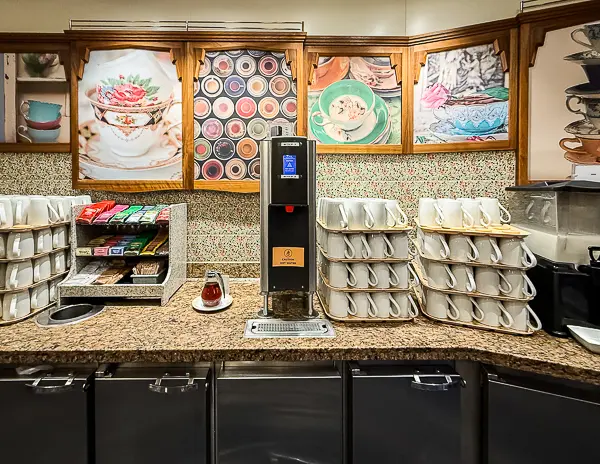 Self-serve station at Café Promenade on Quantum of the Seas, with stacked coffee cups, tea bags, stirrers, and a hot water dispenser arranged on a granite counter.