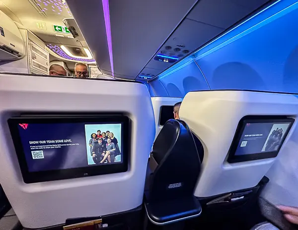 Delta First Class seats with personal entertainment screens, soft blue ambient lighting, and spacious cabin layout during boarding.