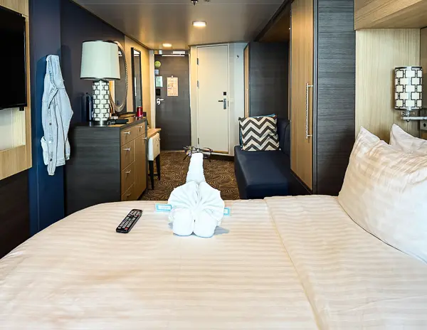 View inside Royal Caribbean’s Quantum of the Seas balcony cabin 6560, showing the bed with a towel animal, vanity area, couch, and entryway.