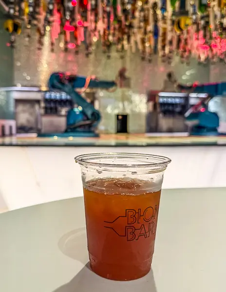 Mai Tai from the Bionic Bar on Quantum of the Seas, sitting on a table with the robot bartenders and illuminated bar background behind it.