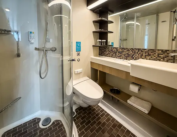 Bathroom in Quantum of the Seas balcony cabin 6560, showing the rounded shower, toilet, long counter, shelving, and mirror.