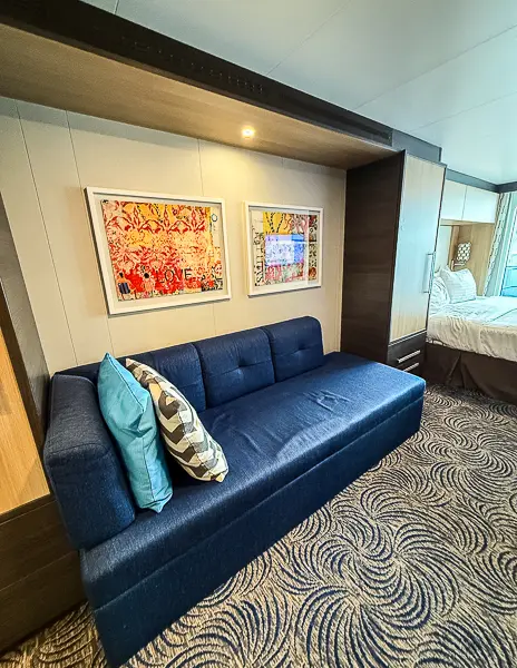 Sofa and artwork inside balcony cabin 6560 on Royal Caribbean’s Quantum of the Seas, with part of the bed area visible in the background.
