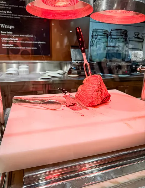Carving station at Café Two70 on Quantum of the Seas, showing a roast beef slab under heat lamps with carving tools on the cutting board.