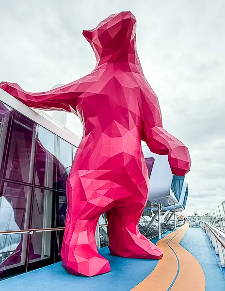 Large pink geometric bear statue known as Felicia on the outdoor deck of Royal Caribbean’s Quantum of the Seas, positioned beside the running track with cloudy skies overhead.
