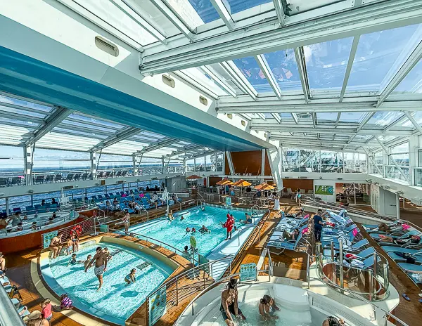 Enclosed pool area on Quantum of the Seas with hot tubs, loungers, and families enjoying the space under the retractable roof.