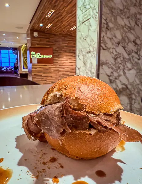 Royal Caribbean’s signature Kummelweck roast beef sandwich served at Café Two70 on Quantum of the Seas, shown on a plate with the café entrance in the background.