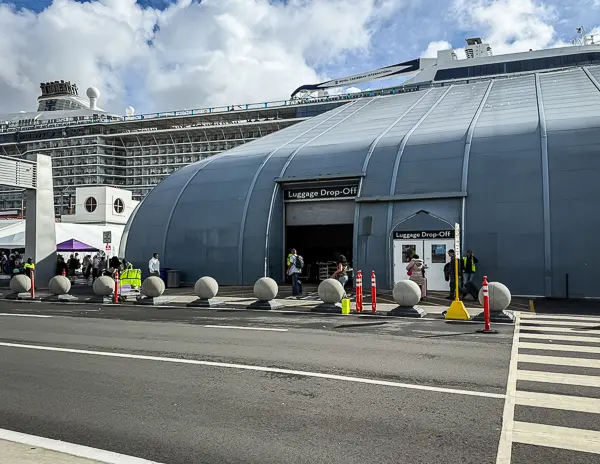 Luggage drop-off area at the Port of Los Angeles in San Pedro, with Quantum of the Seas docked behind the terminal and staff assisting passengers outside.