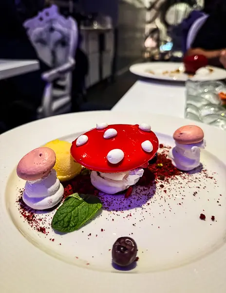 Whimsical mushroom-themed dessert at Wonderland on Quantum of the Seas, with meringue pieces and bright red topping on a white plate.