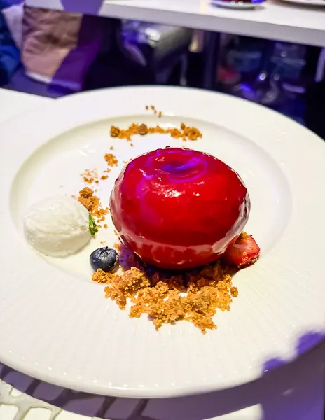 Red apple–shaped dessert at Wonderland on Quantum of the Seas, plated with crumbs, fruit, and a scoop of sorbet.