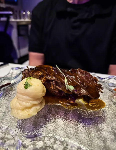 Short rib entrée at Wonderland on Quantum of the Seas, served with a small swirl of mashed potatoes on a textured glass plate.