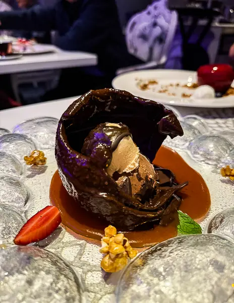 The World dessert at Wonderland on Quantum of the Seas, cracked open to reveal chocolate and caramel layers on a glass plate.